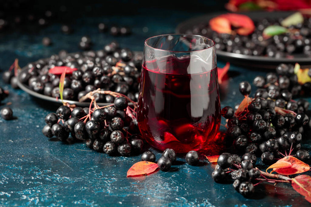 Black chokeberry juice and fresh berries on a dark blue background. - 写真・画像