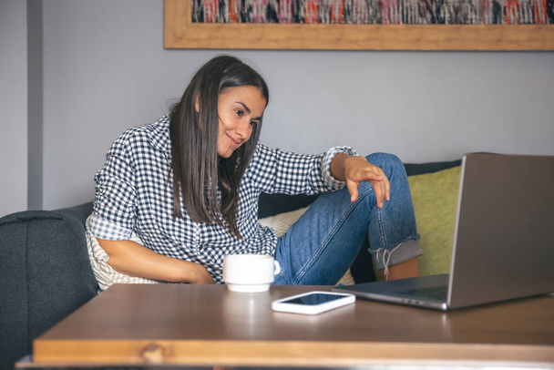 A young woman working on a laptop at home on the couch, the concept of remote work, freelancing. - 写真・画像