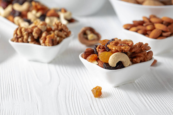 Meng noten en rozijnen op een witte houten tafel. Gepresenteerde rozijnen, walnoten, hazelnoten, cashewnoten, pecannoten en amandelen. - Foto, afbeelding