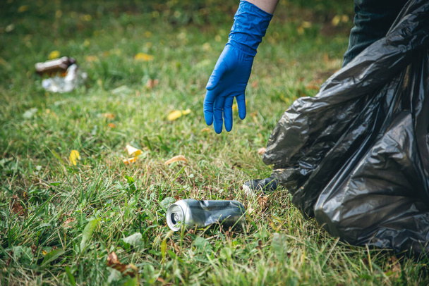 Рука людини в рукавичці очищає сміття в лісі, догляд за навколишнім середовищем та екологією
. - Фото, зображення