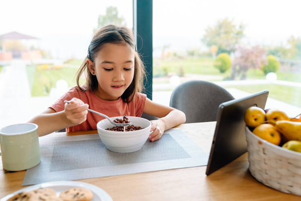 Asian girl using tablet computer while having breakfast at home - Fotoğraf, Görsel