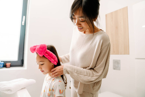 Asian mother and her daughter standing together in bathroom at home - Valokuva, kuva