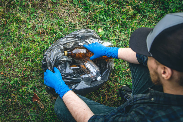 A man puts a plastic bottle in a garbage bag, the concept of forest cleaning and love for nature. - Foto, Bild