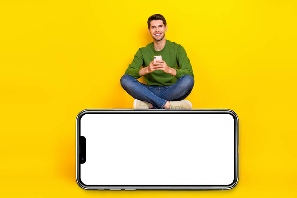 Photo of charming pretty guy wear green sweater typing modern device empty space isolated yellow color background. - Foto, imagen