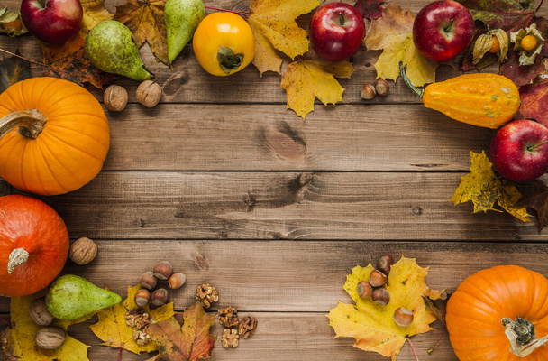 Variety of gourds, squash types and pumpkins. Flat lay composition frame with walnuts, hazelnuts, apples, kaki persimmon, pears and autumn leaves. Copy space on wooden background. - Foto, Imagem