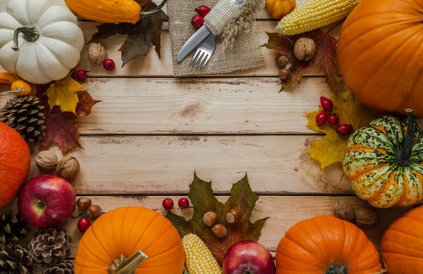 Autumn flat lay composition frame with copy space on wooden background. Pumpkins, cones, leaves, corn on the cob, with fork and knife on a jute material, for Thanksgiving dinner. - Foto, Imagem
