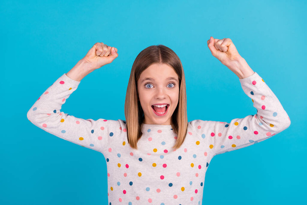Photo of lucky excited little lady dressed dotted pullover shouting rising fists isolated blue color background. - Foto, afbeelding