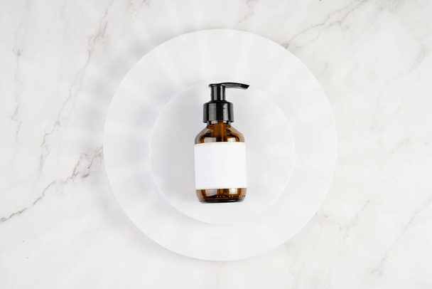 A mock-up of a brown cosmetics bottle with dispenser and white label on white round podiums on marble background, top view - Foto, Imagem