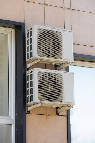 δύο μονάδες κλιματιστικών εξωτερικού χώρου για διάχυση θερμότητας κρέμονται στον τοίχο έξω από το κτίριο. - Φωτογραφία, εικόνα