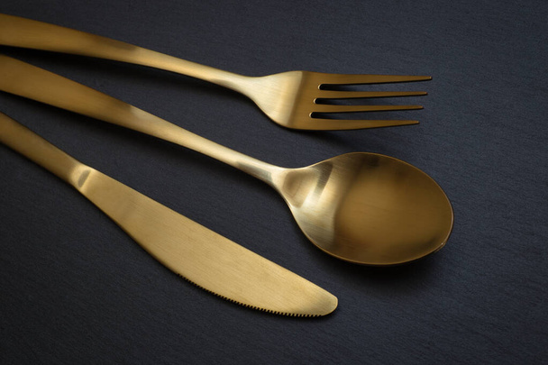 Gold knife, fork and spoon on a black stone background - Food concept photography - Photo, Image
