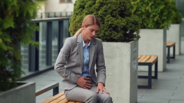 Poor quality food delivery. Middle aged business woman suffering from acute stomach pain, sitting on bench near office and touching her painful belly, slow motion, free space - Video