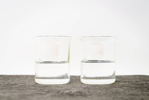 Two beakers with clear liquids and blank labels against white background - Valokuva, kuva