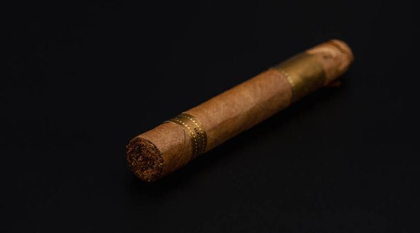 Single cigar. Handcrafted Brown cigar made with real tobacco leaves on dark background. Smoking causes addiction and cancer. Nicotine Damage your health. - Photo, Image