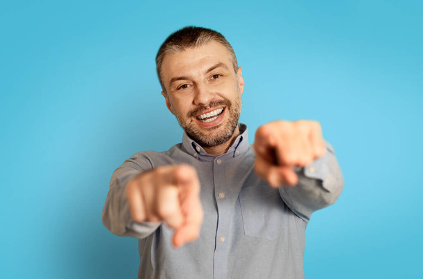 I Choose You. Cheerful Middle Aged Man Pointing Fingers At Camera With Both Hands Posing Standing Over Blue Background, Studio Shot. Look At You Concept. Selective Focus - Foto, afbeelding