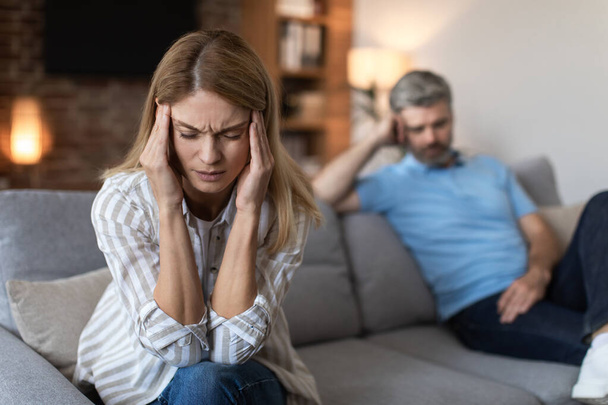 Upset offended mature european husband ignores wife, lady suffers from headache in living room interior. Stress, pressure, negative human emotions, problems in relationships at home and bad news - Photo, Image