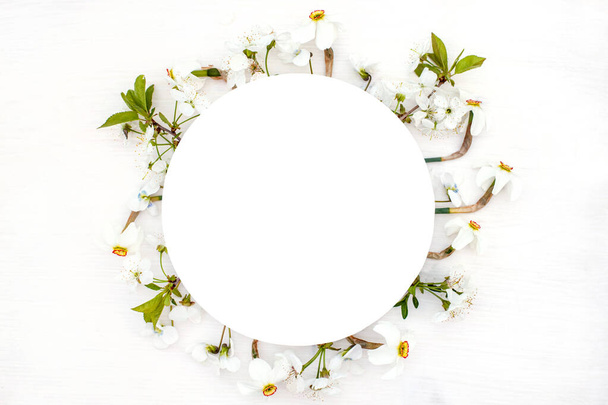 Round frame with spring flowers. fresh cherry blossoms, violets and white daffodils in the form of wreath on wooden background. - Photo, Image
