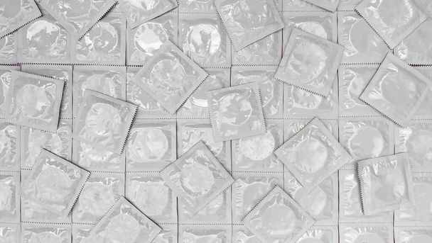 Many white packages of unopened condoms as a background. Using a condom to reduce the chance of pregnancy or sexually transmitted diseases, STDs. The concept of safe sex and reproductive health. - Фото, изображение