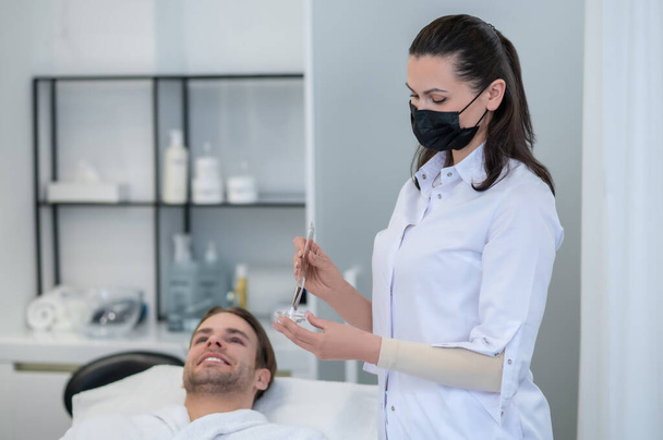 Beauty salon. Cosmetologist applying facial mask to mans face - Foto, Bild
