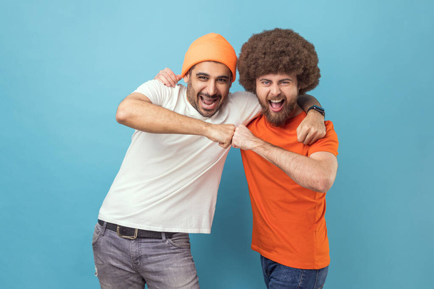 Yes we did. Portrait of two handsome happy excited young adult hipster men celebrating triumph together, showing bro fist, power five sign. Indoor studio shot isolated on blue background. - Фото, зображення