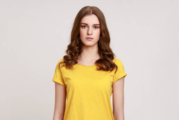 Portrait of pretty serious bossy brown haired woman of young age in yellow casual T-shirt, looking at camera with suspicion and accusing. Indoor studio shot isolated on gray background. - Fotoğraf, Görsel