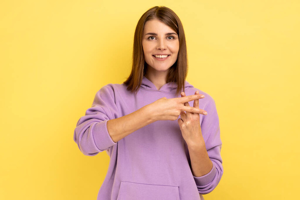 Hash symbol. Portrait of attractive woman making hashtag gesture and smiling, looking at camera, popular blogger, wearing purple hoodie. Indoor studio shot isolated on yellow background. - Foto, immagini