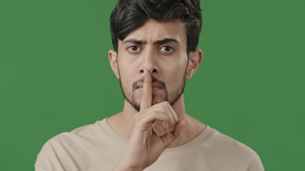 Close up serious arab guy looking at camera face young hispanic man hold index finger near mouth make silence shows gesture secret sign forbid speaking mystery gossip confidential information concept - Video