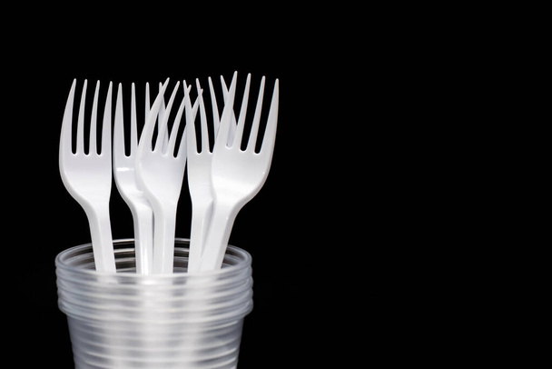 Disposable plastic forks and glasses on a black background. Free space for text. Disposable utensils for eating and drinking at a picnic or outdoors. Taking care of the environment with organic dishes - Fotoğraf, Görsel