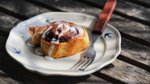 A close-up of a delicious freshly baked cinnamon rolls on a plate next to a fork on a wooden surface - Foto, Imagem