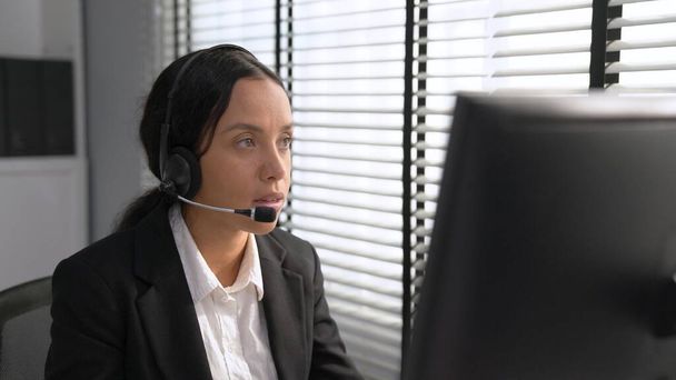 Competent female operator working on computer and talking with clients. Concept relevant to both call centers and customer service offices. - Foto, afbeelding