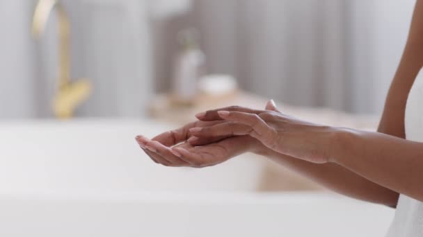Luxury nourishing cosmetics. Close up shot of unrecognizable black lady rubbing cream or foam in palm, standing at bathroom interior, tracking shot, free space - Video, Çekim