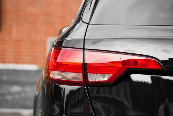 A closeup shot of the red tail light of a black car with a wall in the background - Fotografie, Obrázek