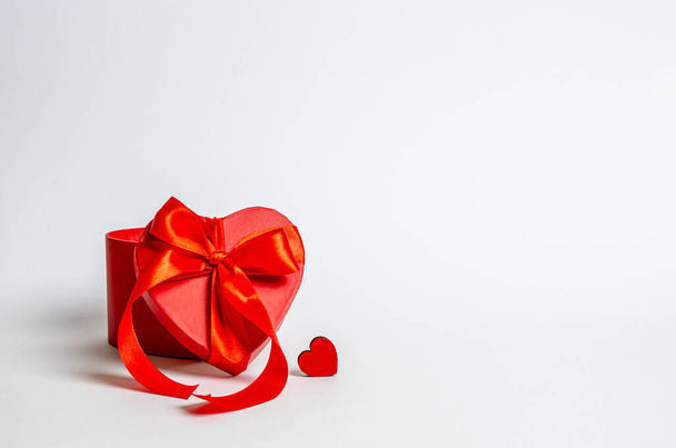 Red gift box with a ribbon and a small heart on a white background. Love concept, congratulations, copy space, banner. Close-up - Photo, Image