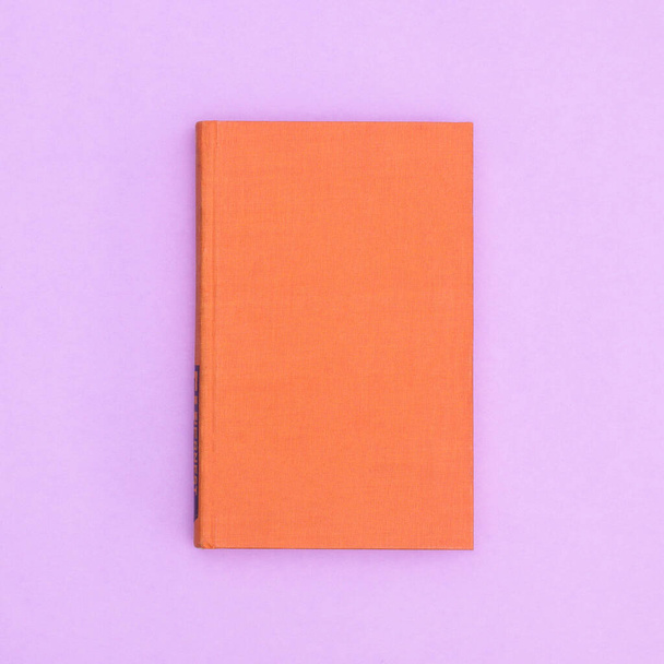 Orange hardcover vintage book on pastel purple background. Flat lay copy space - Photo, Image