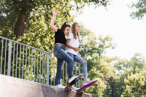 Skater children girls reade to ride on penny board on skate sport ramp at sunset together. Sports equipment for kids. Active teenager with pennyboard on skate park playground - Foto, Bild