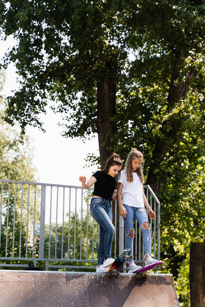 Children friendship. Girls friends ready for ride on penny board on skateboard park playground. Sports equipment for kids. Extreme lifestyle - Zdjęcie, obraz