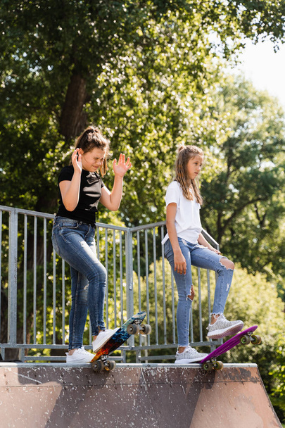 Children friendship. Girls friends ready for ride on penny board on skateboard park playground. Sports equipment for kids. Extreme lifestyle - 写真・画像