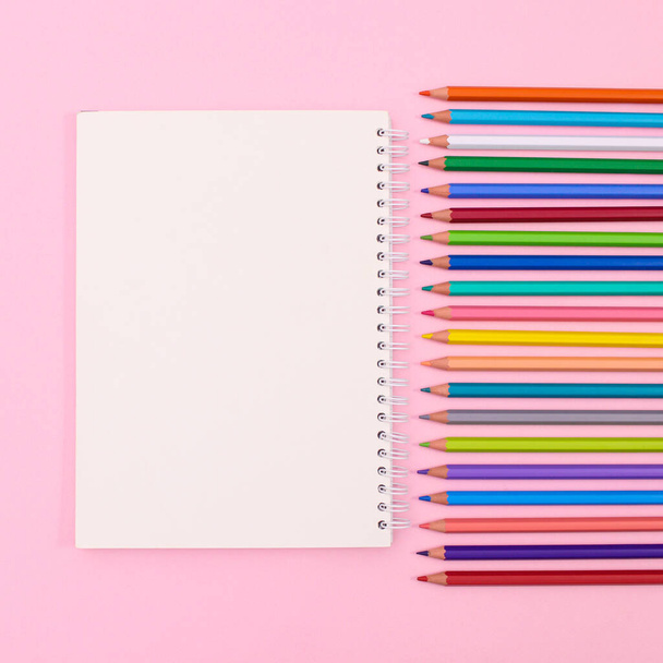 Colorful wooden pencils with open notebook copy space on pastel pink background. Flat lay - Foto, Bild