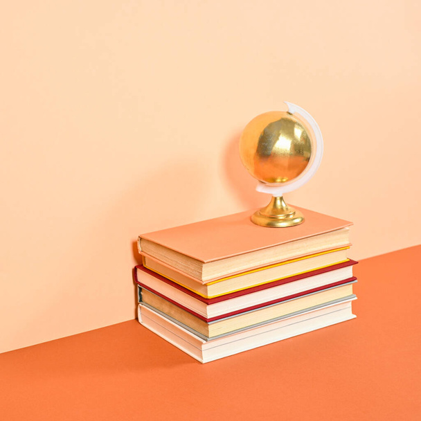 Golden Earth globe on hardcover vintage books on pastel two shade  orange background. Flat lay - 写真・画像