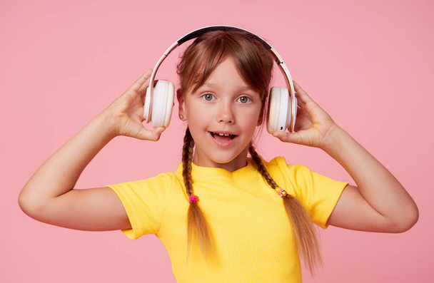 Funny child girl in yellow posing isolated on pink background. Mock up copy space. Listen music with headphones - Foto, immagini