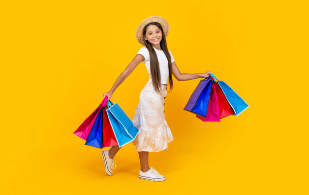 smiling teen girl with shopping bags on yellow background. full length. - Valokuva, kuva