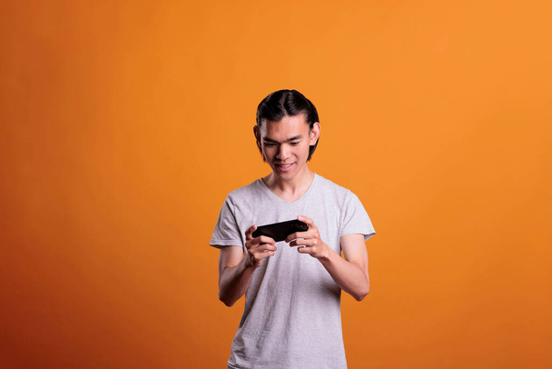 Excited teen playing video games on phone, young asian man having fun, enjoying online mobile videogames. Internet leisure activity, cheerful gamer using smartphone entertainment application - Photo, Image