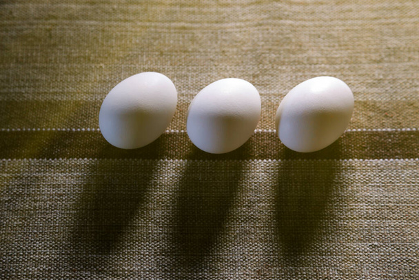 drei weiße Eier gruppiert auf Stoff und weiche Seitenbeleuchtung - selektiver Fokus - Foto, Bild