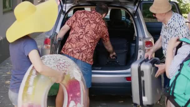 Happy people loading vehicle with luggage and trolleys while going on weekend citybreak together. Big family packing voyage luggage in car trunk while getting ready for summer field trip. - Materiał filmowy, wideo
