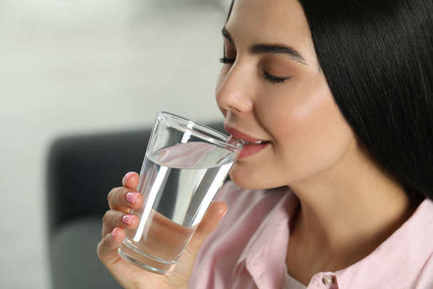 Young woman drinking water indoors, closeup. Refreshing drink - 写真・画像