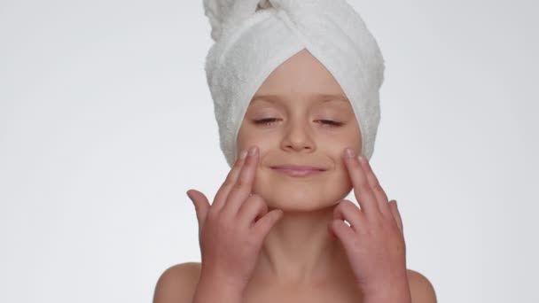 Lovely young child girl after bath in towel on head applying cleansing moisturizing cream. Teenager kid face skincare healthy treatment, natural creme cosmetics. Female portrait. Perfect fresh clean - Záběry, video