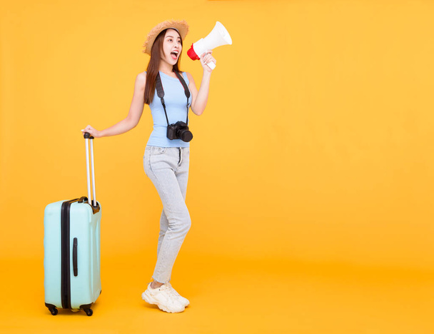 Ευτυχισμένη νεαρή γυναίκα με αποσκευές και κρατώντας μεγάφωνο απομονωμένο σε κίτρινο φόντο, καλοκαίρι, ταξιδιωτική έννοια. - Φωτογραφία, εικόνα