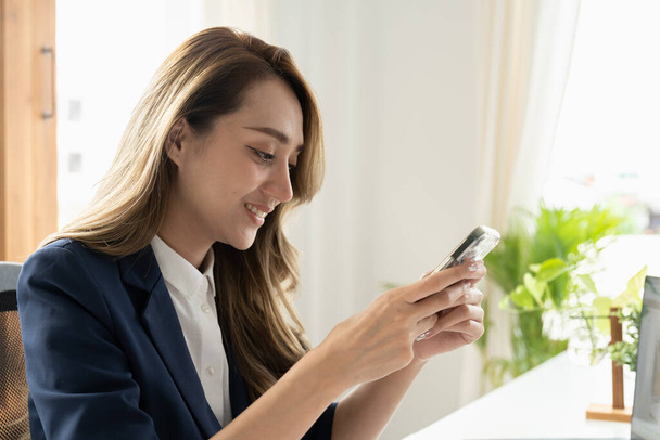 Lächelnde Geschäftsfrau mit Telefon im Büro. Kleinunternehmerin schaut auf ihr Handy und lächelt - Foto, Bild