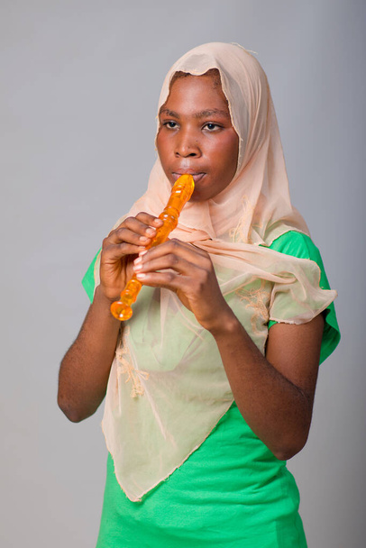 African Nigerian Muslim lady, girl or music student wearing an hijab head scarf and blowing musical instrument called flute - Photo, image