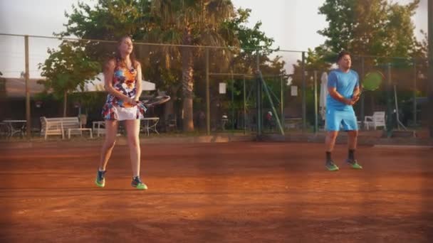 A young man and woman on tennis training - view through the net. Mid shot - Filmati, video