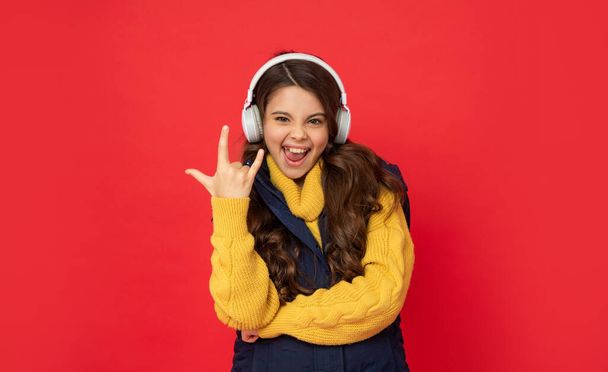 modern life in childhood. cool gesture. happy child listen music in headphones. kid wear warm clothes. express positive emotion. winter fashion. teen girl in hat and earphones. - 写真・画像